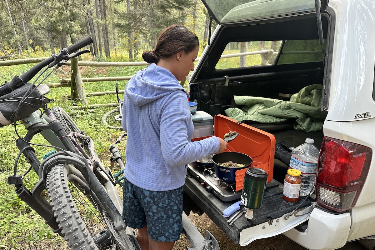 A woman wearing a fleece pullover makes dinner on the tailgate of a truck