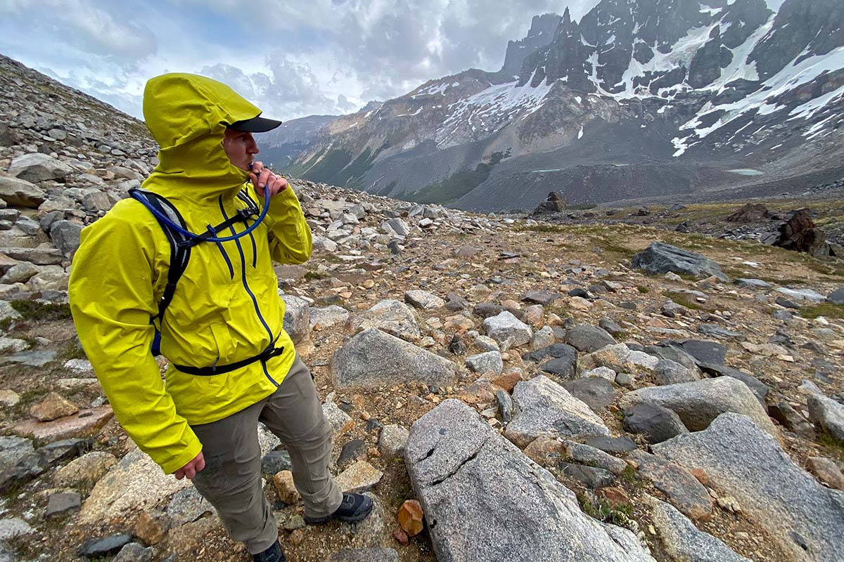 Day Hiking Checklist (man wearing rain jacket taking water break under stormy skies in the mountains)