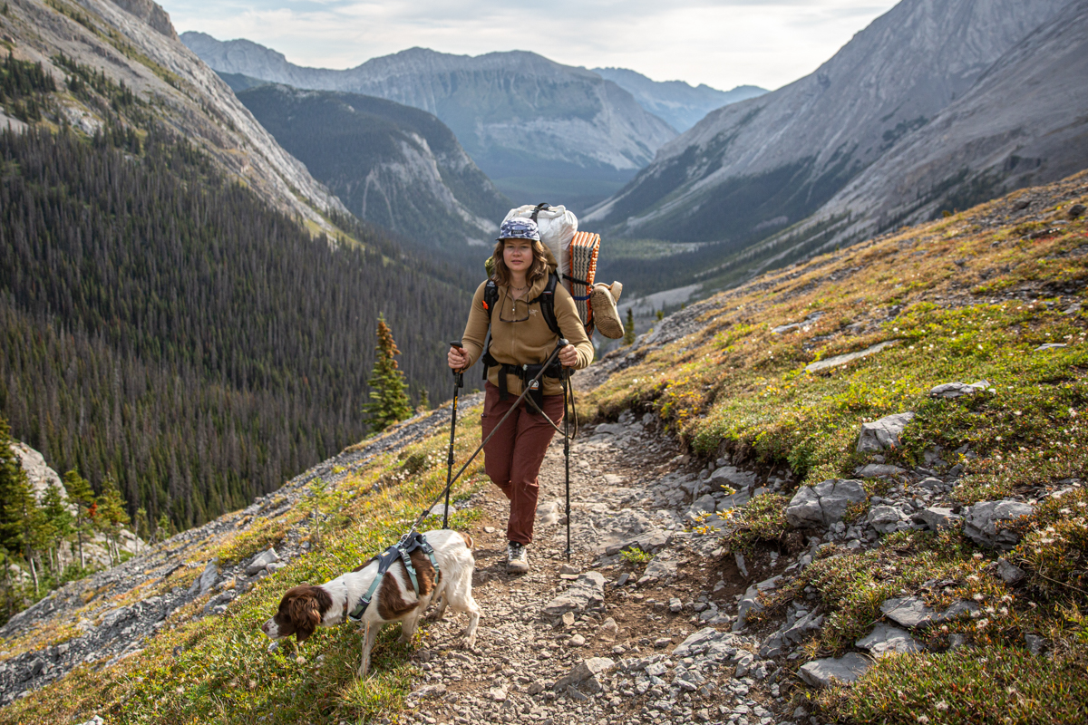 A woman hiking up a rocky trail with a dog while wearing a brown fleece jacket