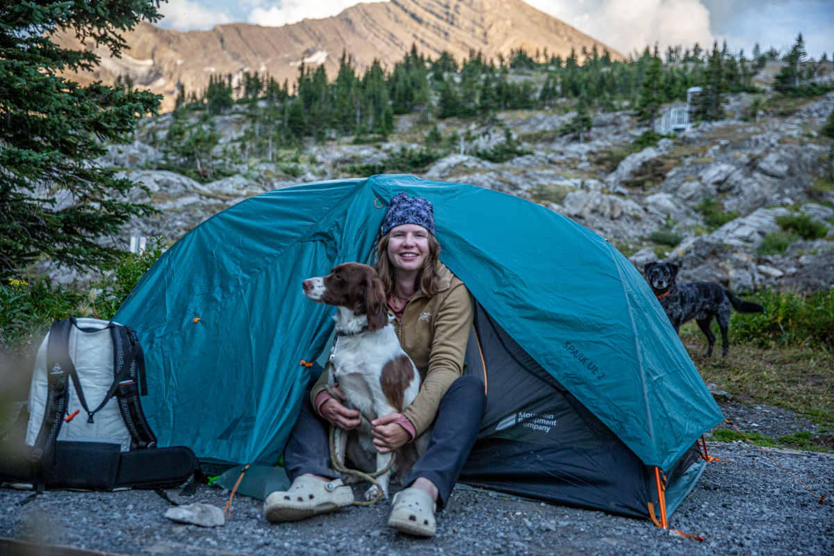 A woman hugging her dog while sitting in the vestibule of a tent and wearing a brown fleece jacket