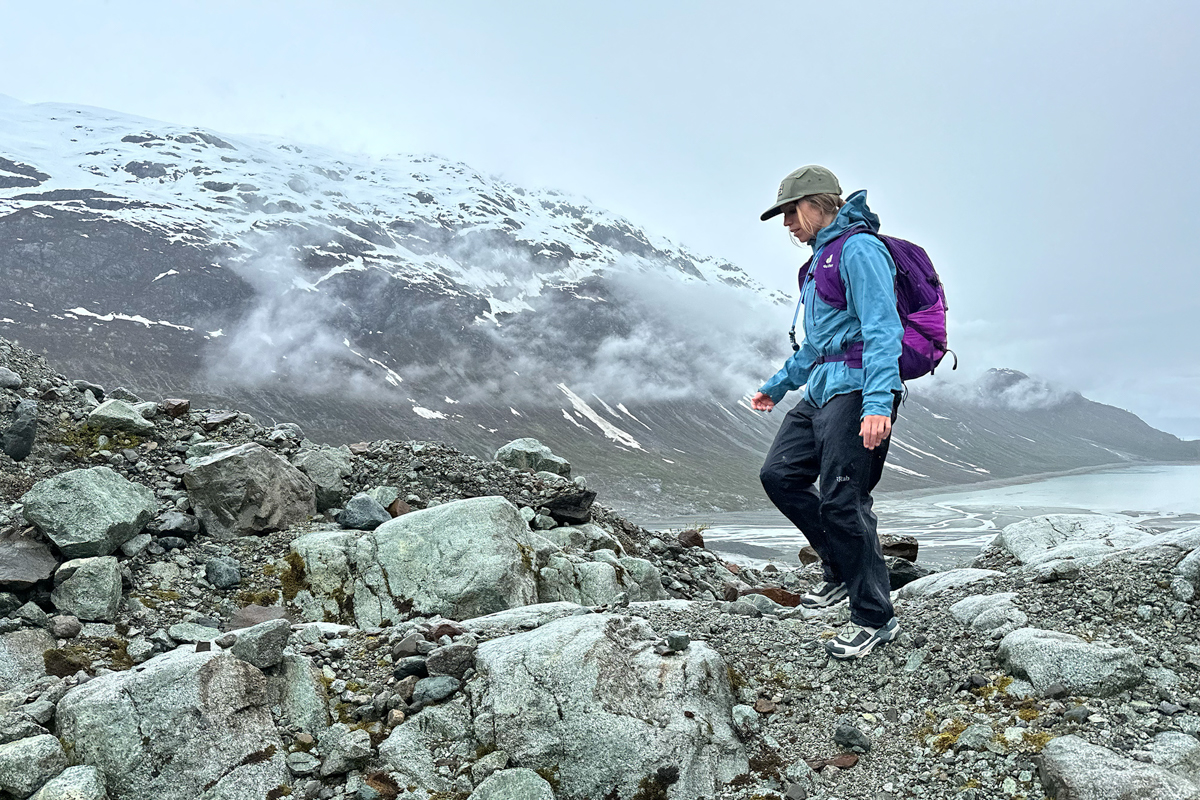 A woman hiking in a rocky and glacial landscape in a purple daypack