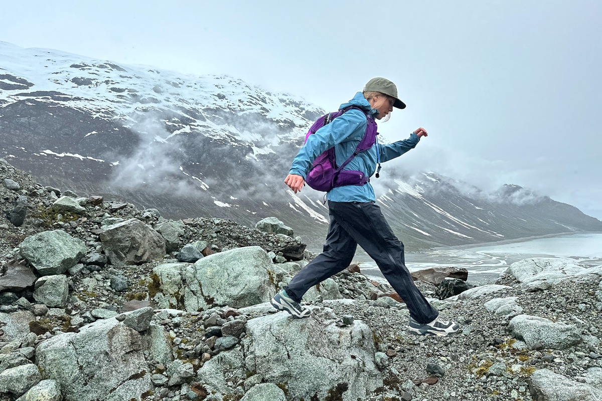 A woman stepping quickly between boulders while waering a purple daypack