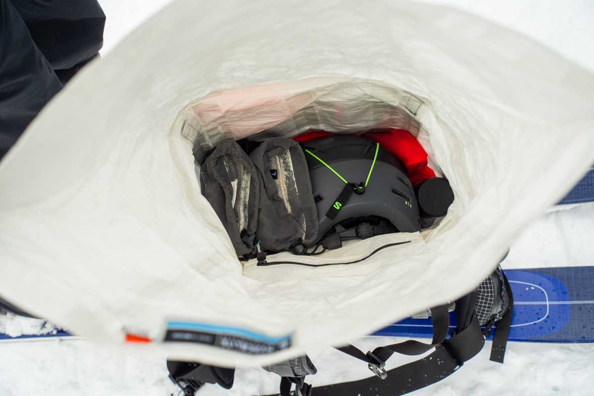 A close up of a helmet and pair of gloves carefully packed inside a white ski backpack