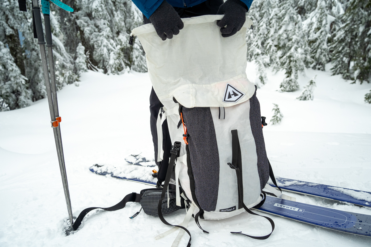 A close up of a white ski backpack sitting on the snow in a forest landscape