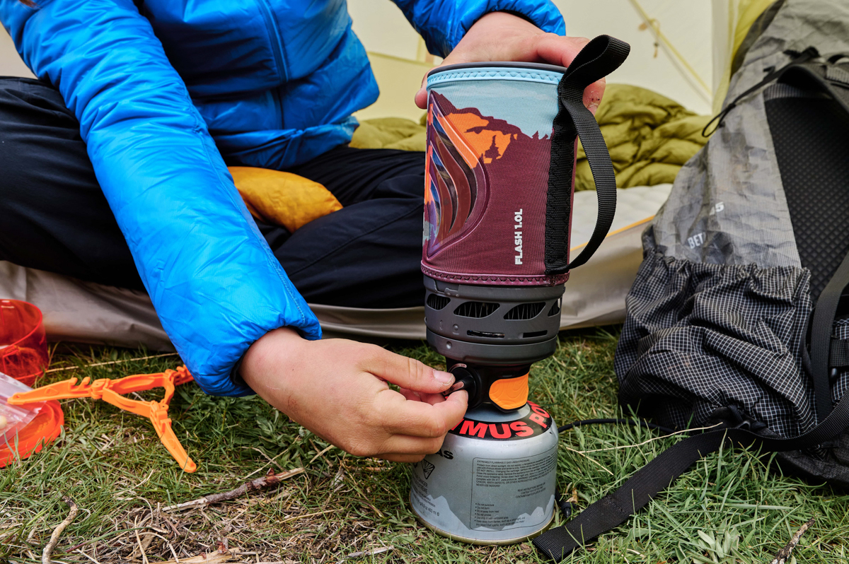 A hand adjusting the temperature regulator on a backpacking stove