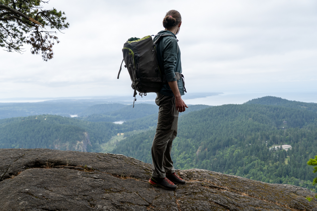 A man standing on a rocky ledge looking out at distance while wearing approach shoes
