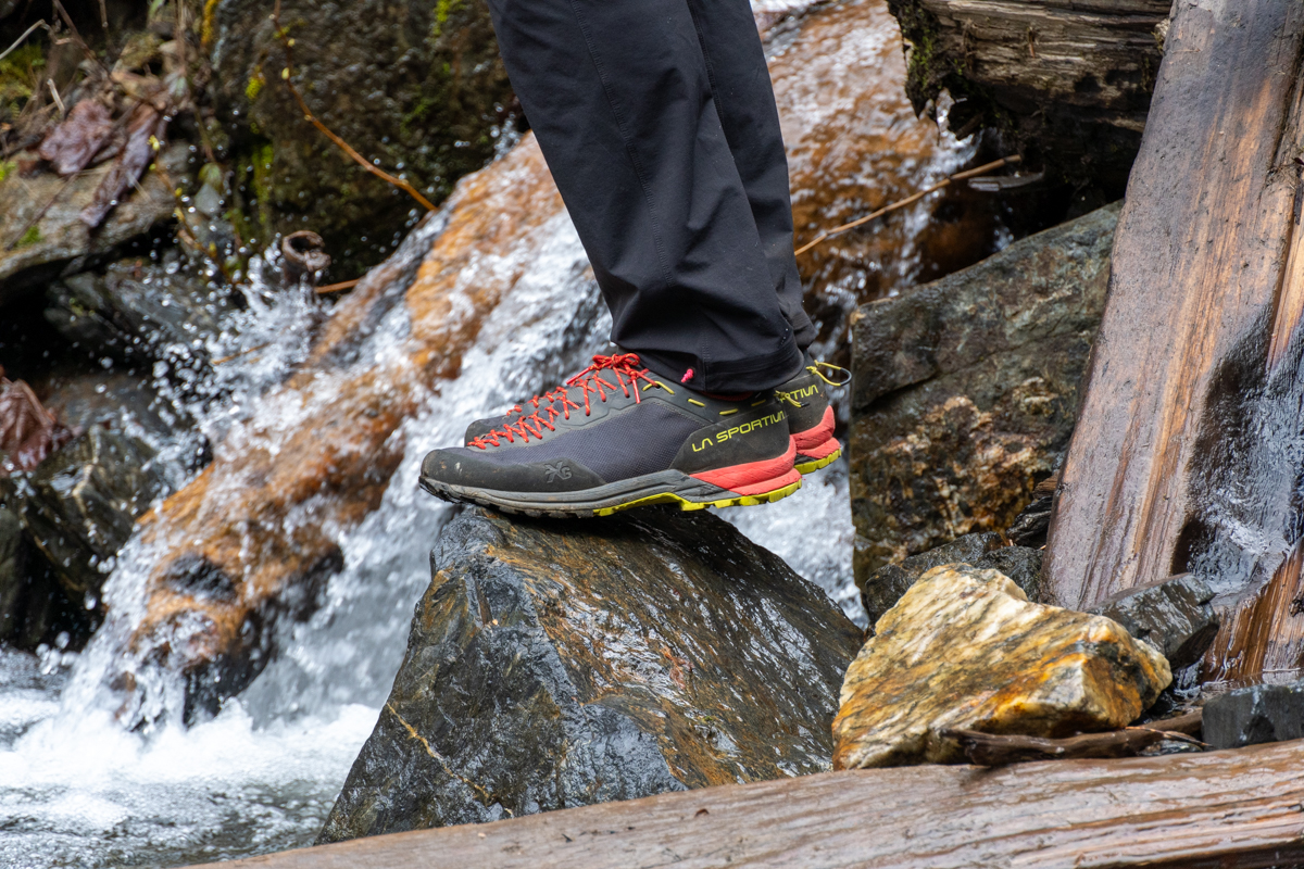 A pair of grey and black approach shoes standing on a wet rock in front of a river