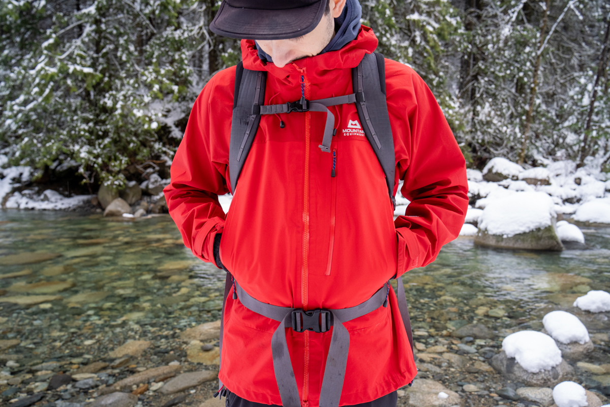 A closeup of a red hardshell jacket in front of a winter river background