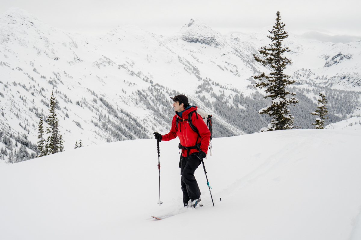 A man backcountry skiing in a snowy landscape in a red hardshell jacket