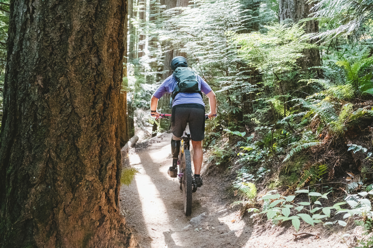 A man biking up a steep forest trail while wearing a green mountain bike backpack