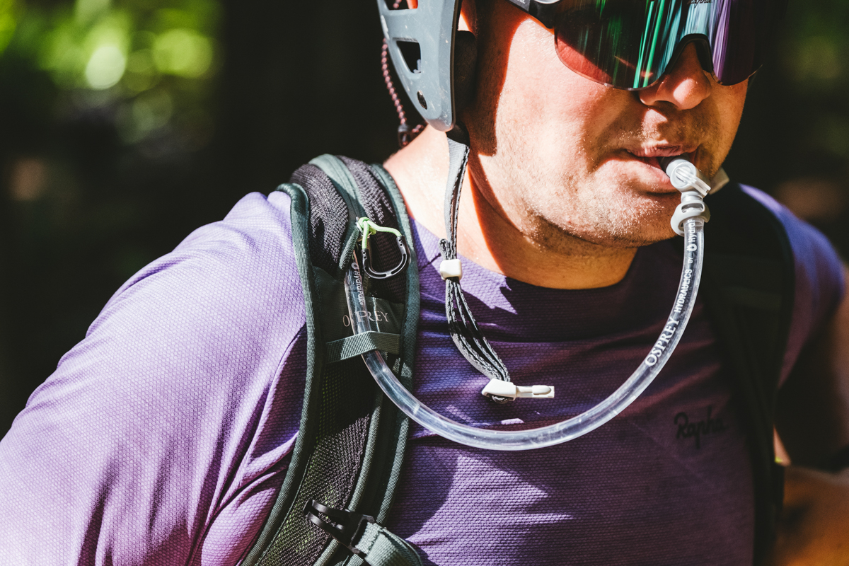 A man drinking out of a hydration hose coming out of a green mountain bike backpack