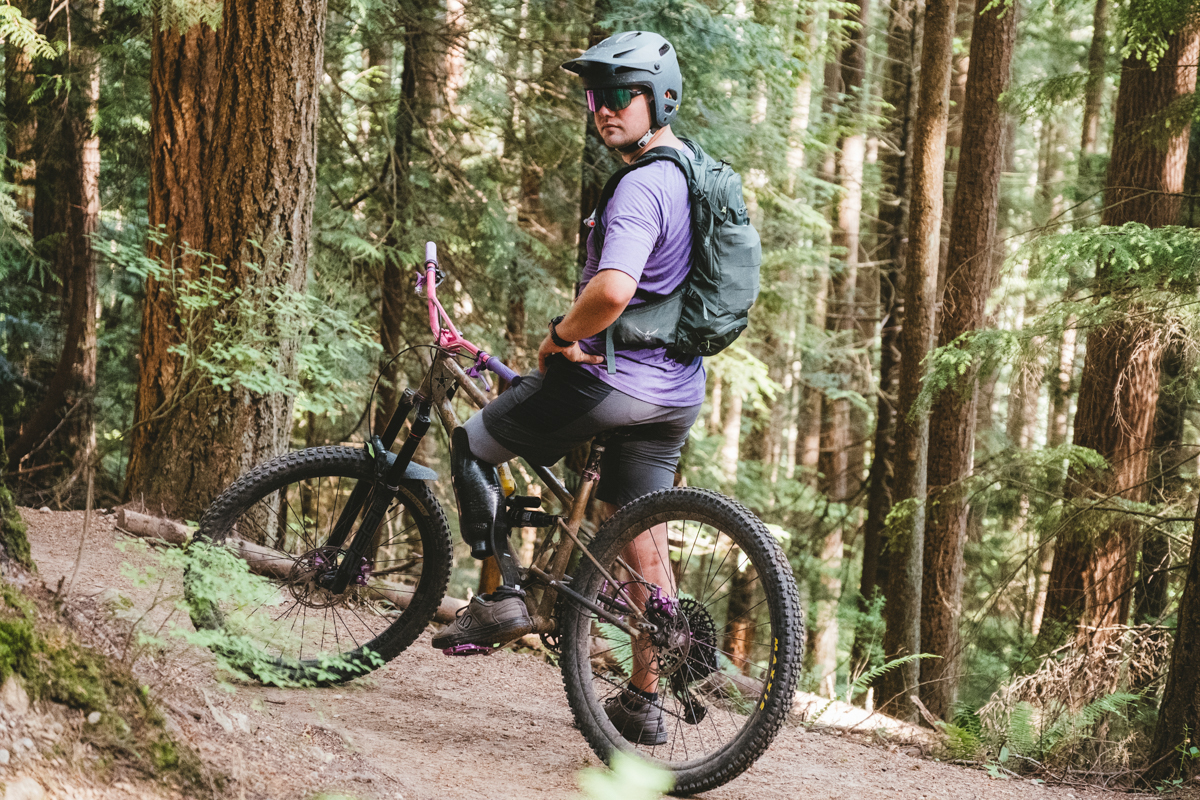 A man sitting on a mountain bike in a forest wearing a green mountain bike backpack