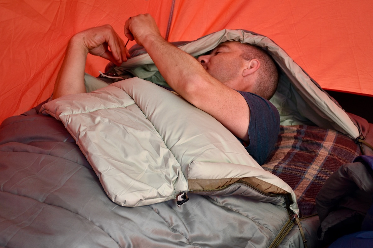 A man adjusts the insulated hood on the REI Co-op Siesta Hooded 20 sleeping bag