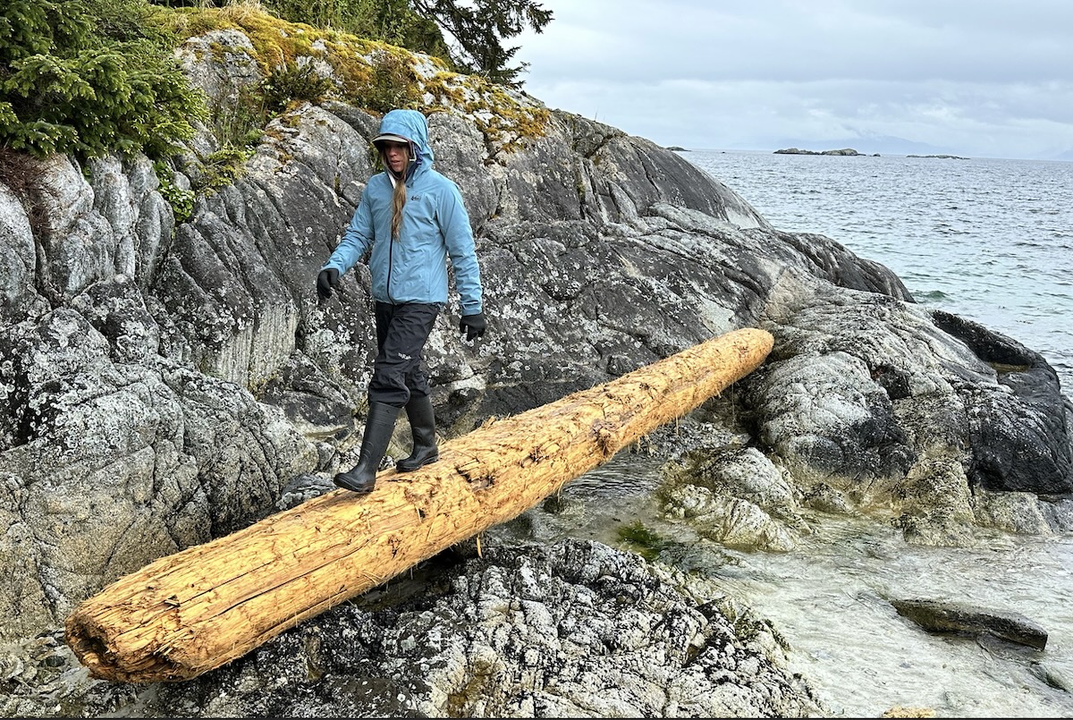 REI co-op XeroCloud rain jacket - walking across a log near the water 
