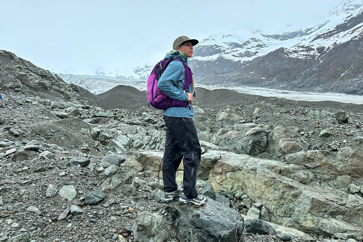 A woman standing on a rock in a rocky costal landscape during a slight drizzle in hiking shoes