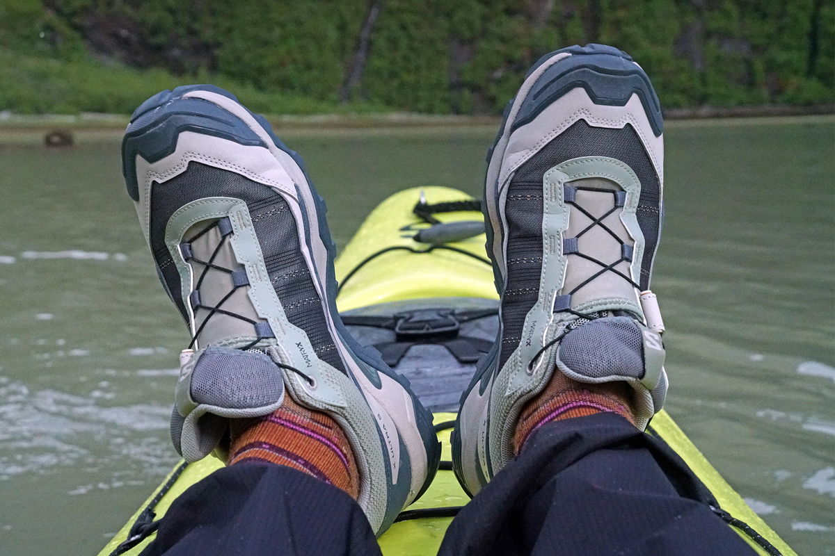 Green and brown hiking shoes sitting at the front of a kayak in water