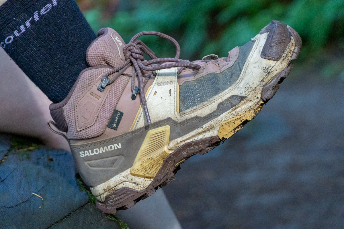 A close up of the side of a brown and pink hiking boot propped up on a log