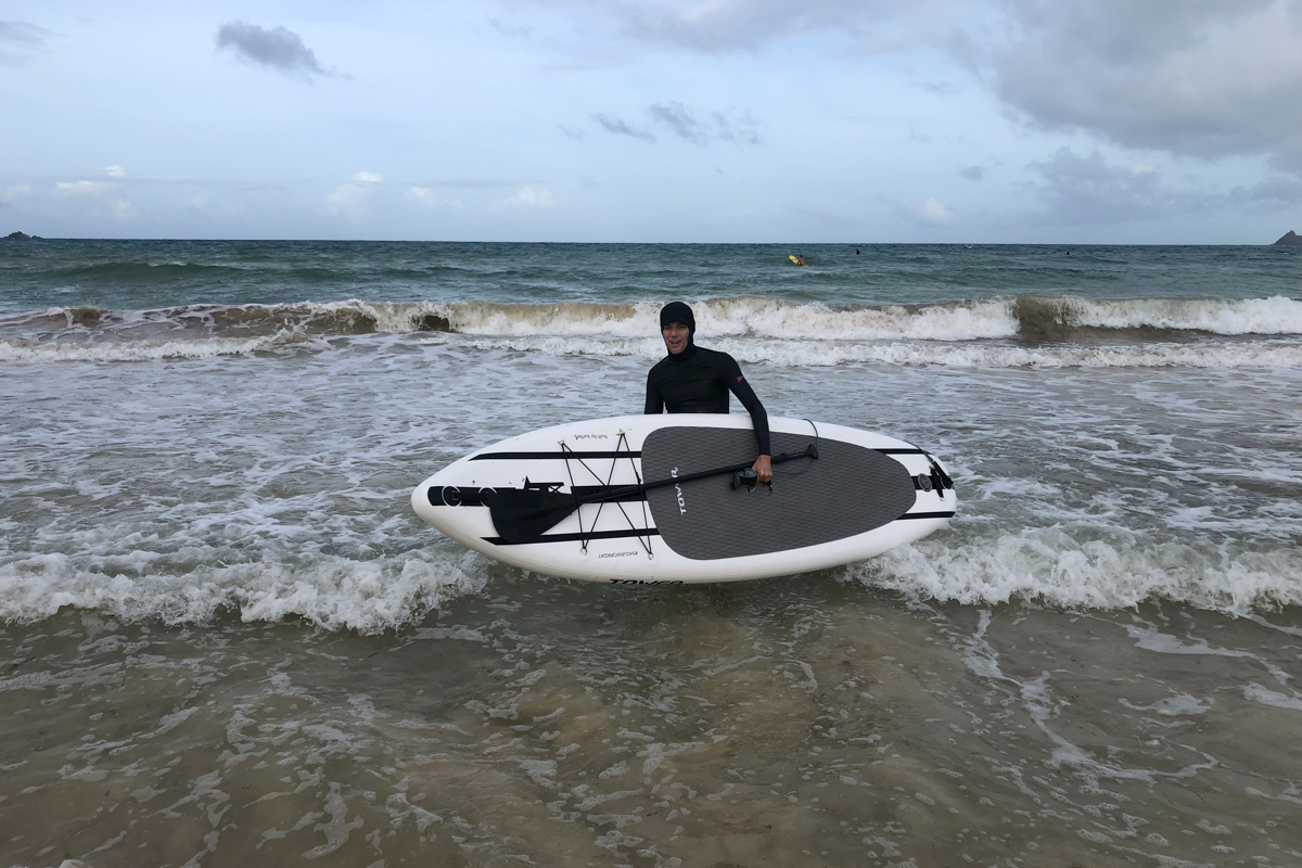 A man in a wet suit holding a paddle board on the edge of the water