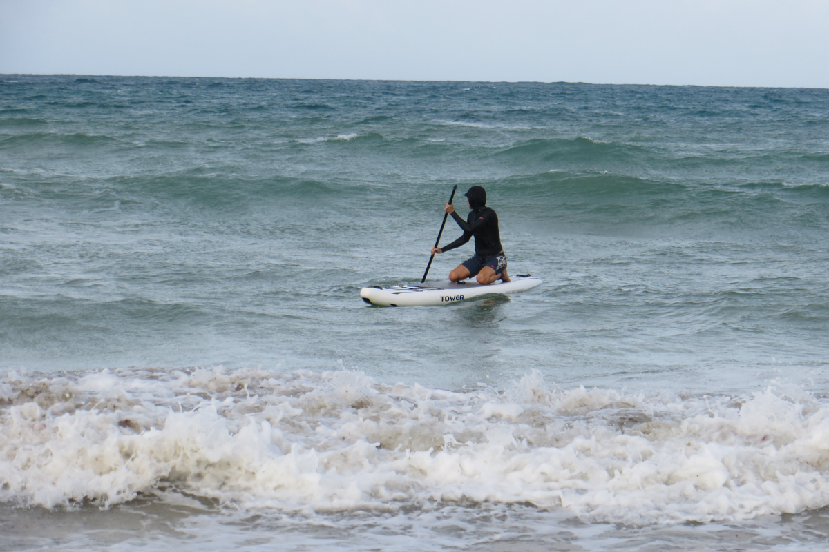 A man in a wet suit kneeling on a paddle board in choppy ocean waves