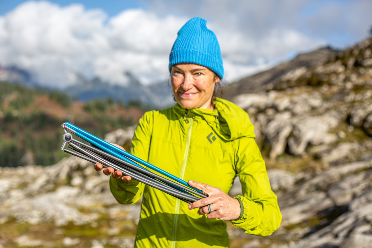 A woman holding backpacking tent poles with a mountainous background