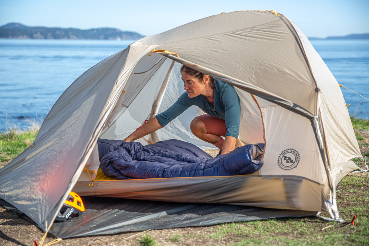A woman putting a sleeping back into a backpacking tent with a water background