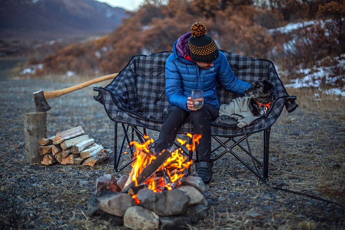 Woman sitting on camp chair beside campfire with dog