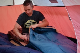 A man zips himself into the Brazos sleeping bag in a camping tent