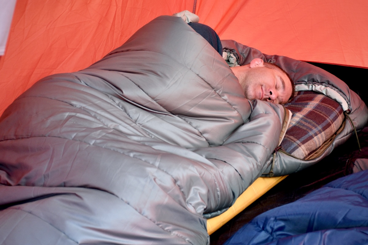 A man drifts off to sleep in a tent in the roomy REI Siesta Hooded 20 sleeping bag
