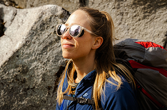 A woman hiking in the mountains wears sport sunglasses.