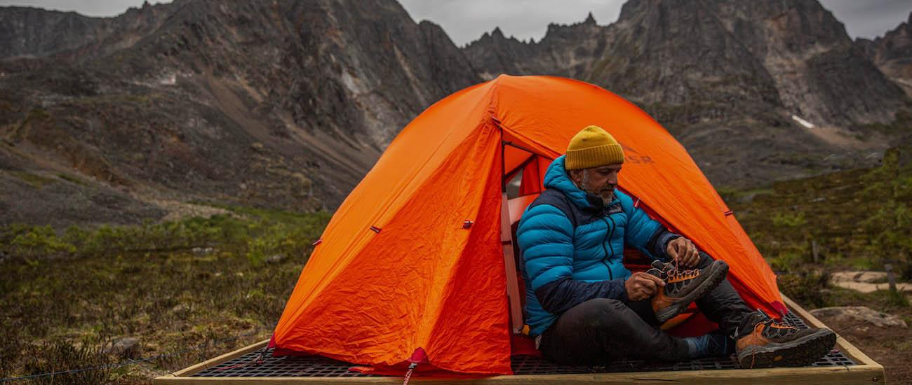 A man sits in the door of a tent putting on his shoes