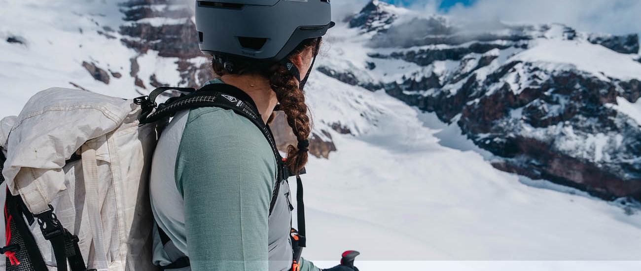 A woman out backcountry skiing looks off toward snow-capped mountains