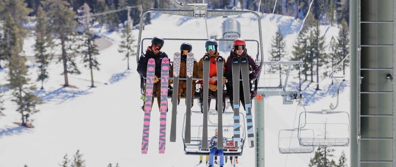 Four people sitting on a ski lift with their legs up to show the underside of their skis