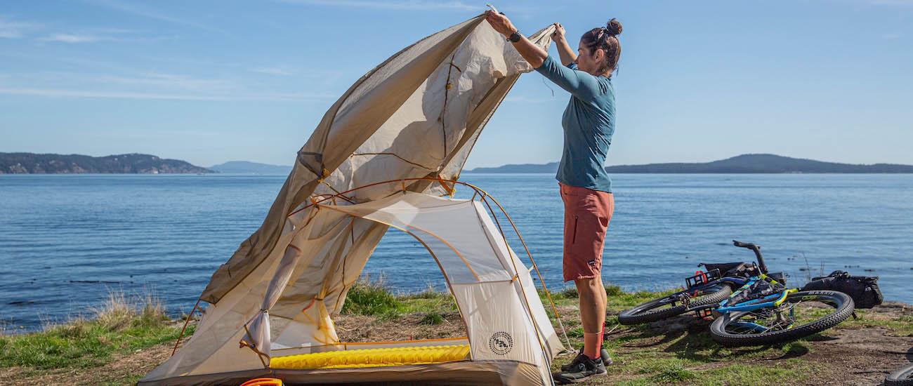 A woman puts the fly over the Tiger Wall tent next to the water with a bike behind her
