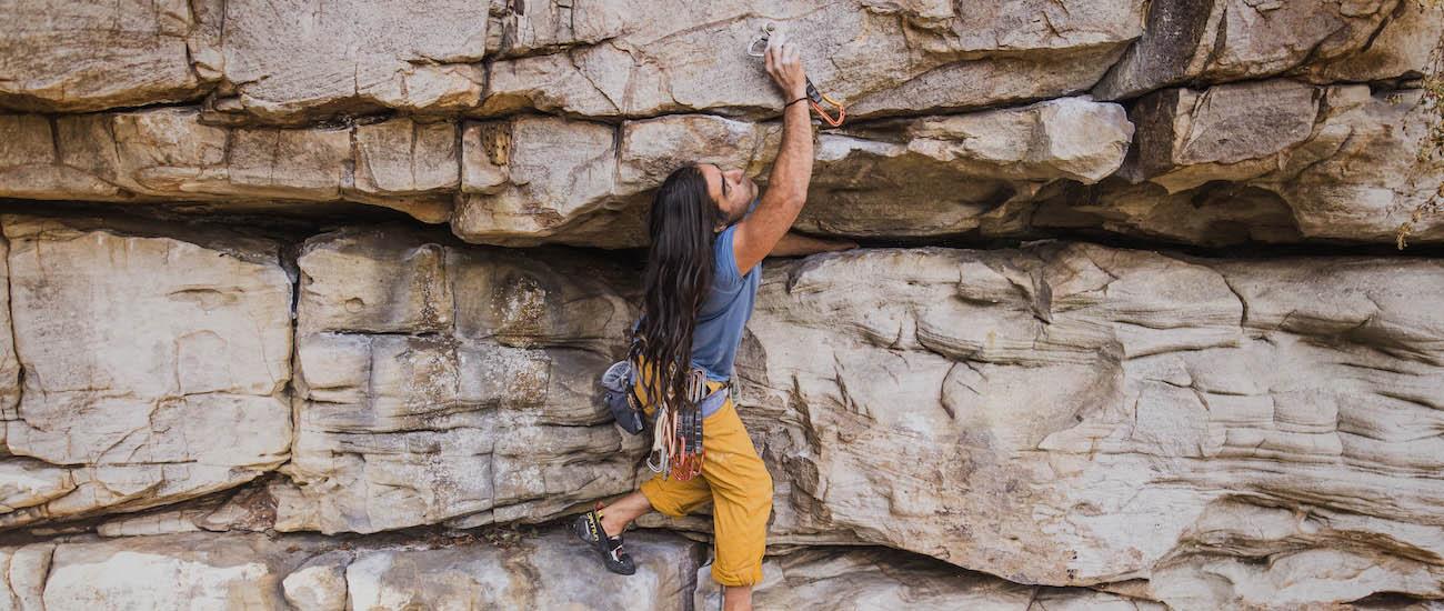 A man reaches up on a rock face to attach a quickdraw to a bolt