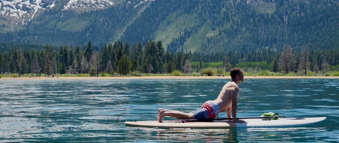 A man performs an upward dog yoga pose on a paddleboard with mountains in the background