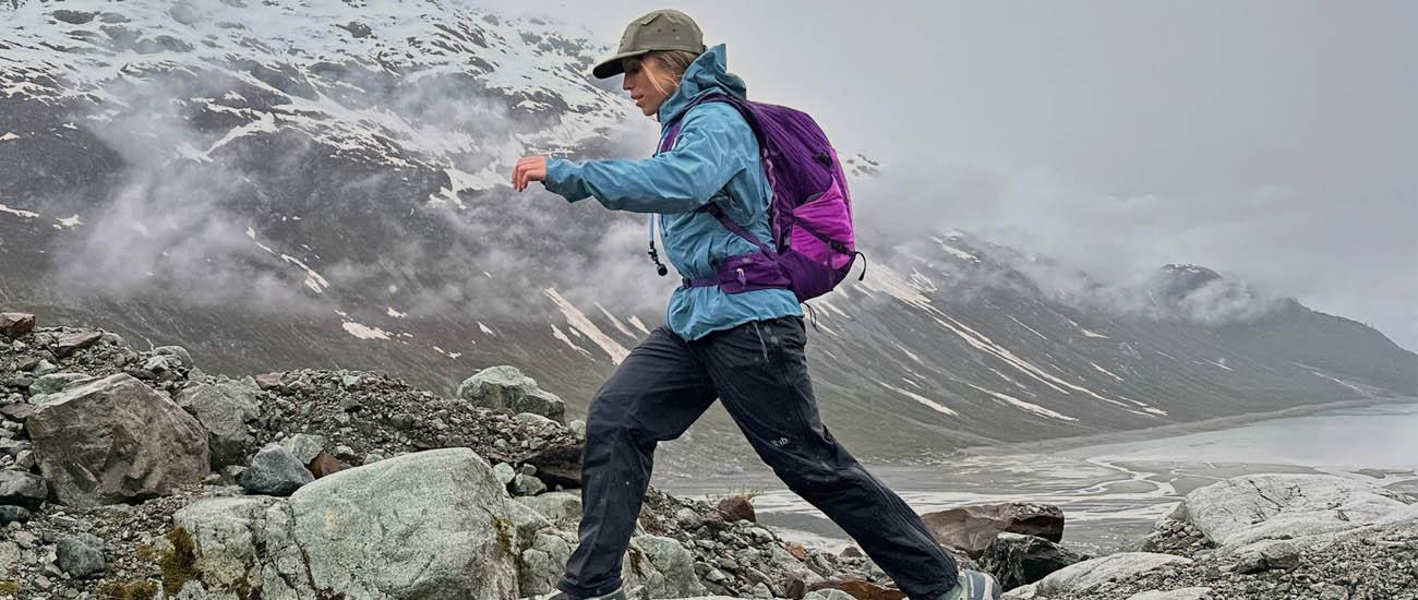 A woman jumps across some rocks on a cloudy day wearing the Deuter Speed Lite Pro backpack