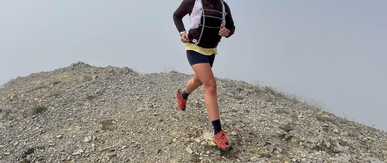 A woman smiling and running down a rock face in the Hoka Speedgoat 2