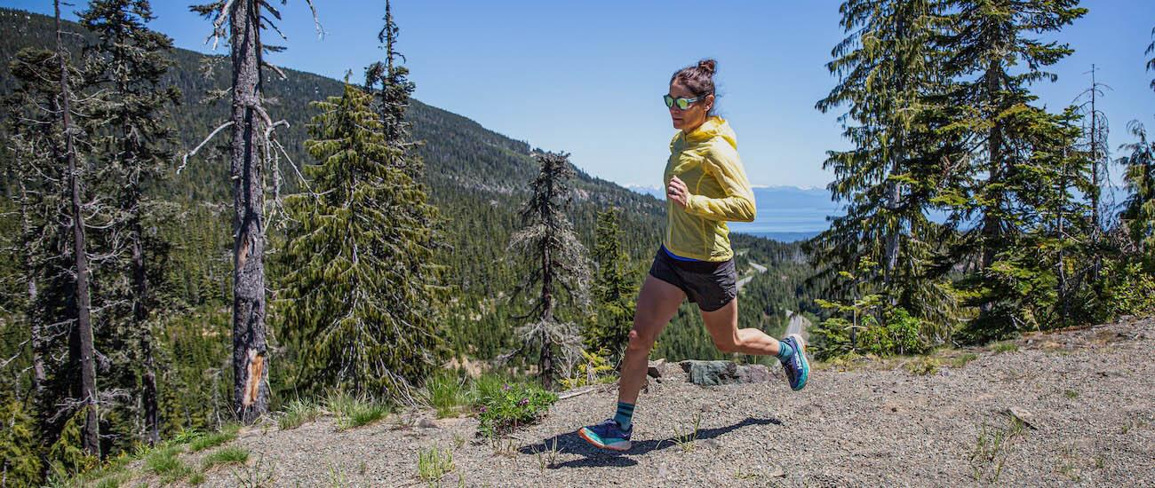 A woman runs on a dirt trail among the trees