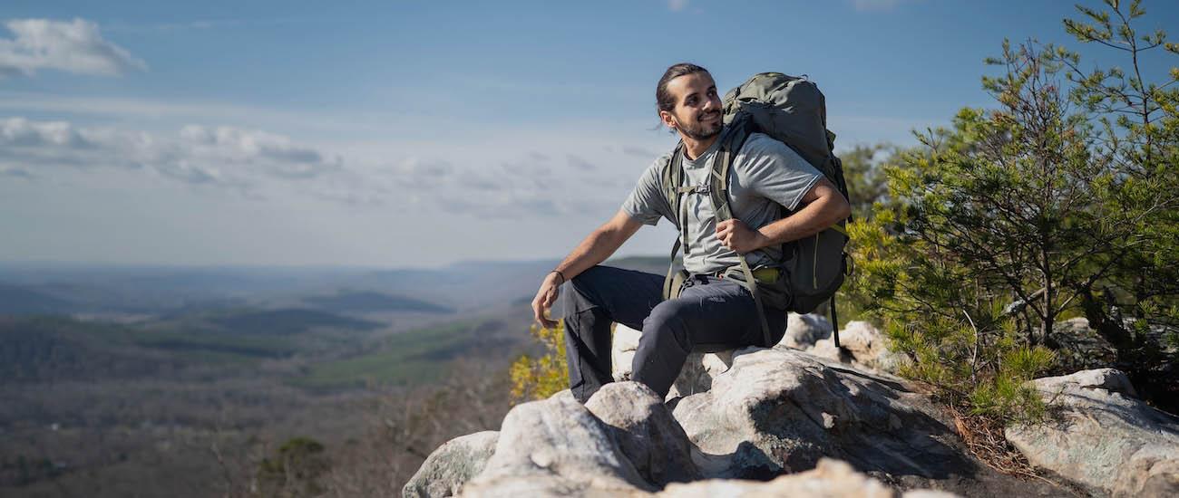 A man with a large backpack sits on a rock with a view from high up