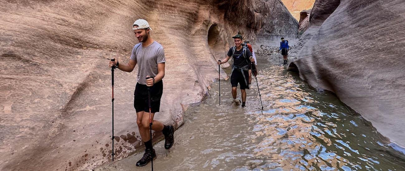 A group of hikers walk through a canyon filled with water