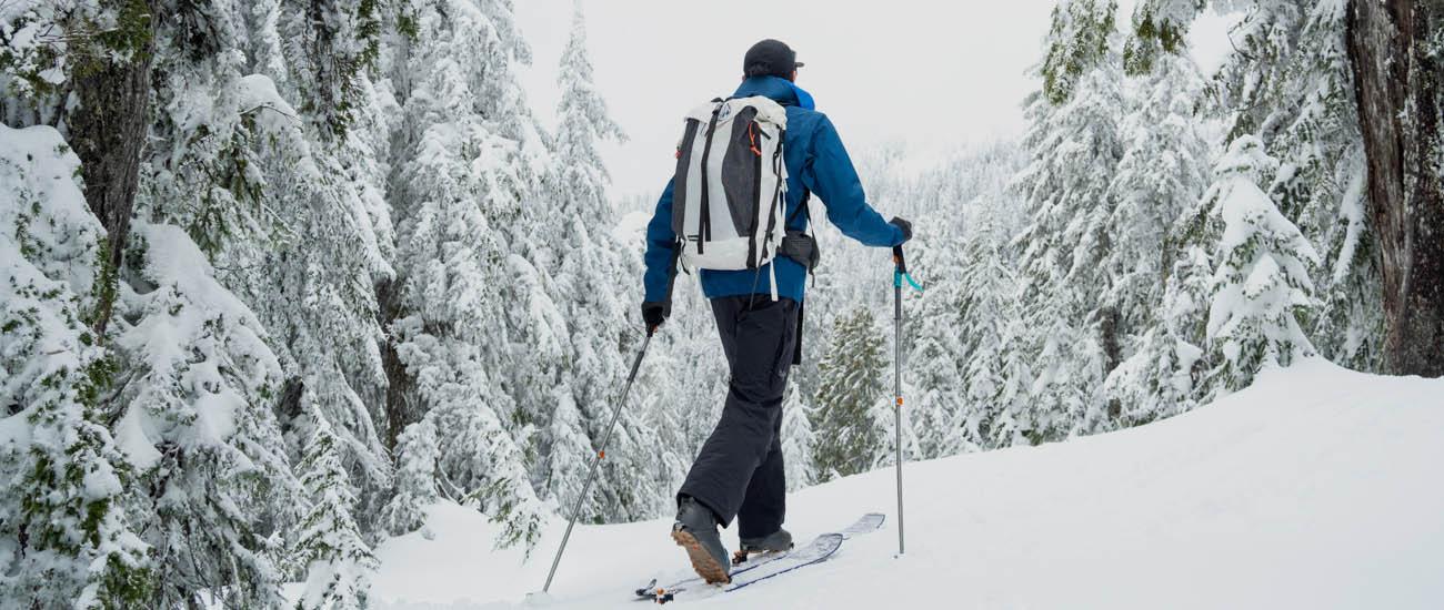 A man skins up a snowy mountain wearing a ski backpack