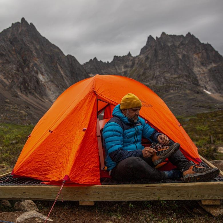 A man sits in the door of a tent putting on his shoes
