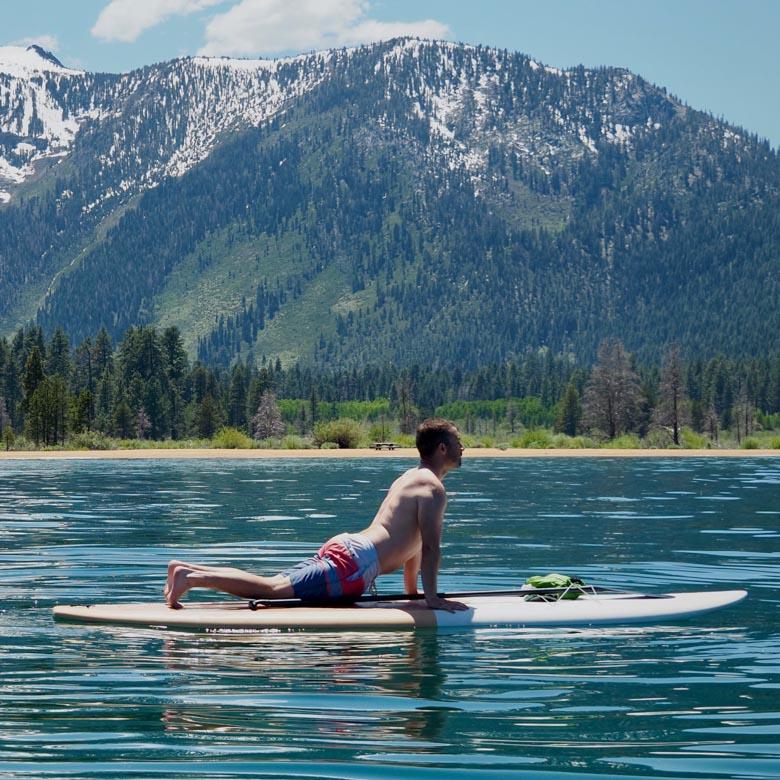 A man performs an upward dog yoga pose on a paddleboard with mountains in the background