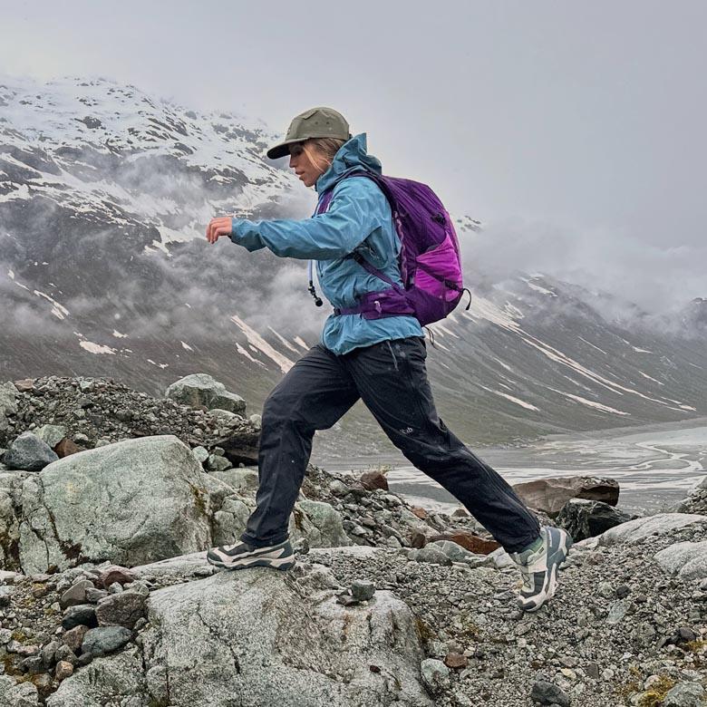 A woman jumps across some rocks on a cloudy day wearing the Deuter Speed Lite Pro backpack
