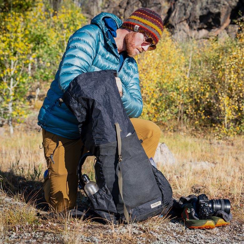 A main packs items into a black backpack while out in the field