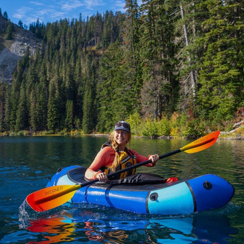 A smiling woman in a packraft paddles in the water
