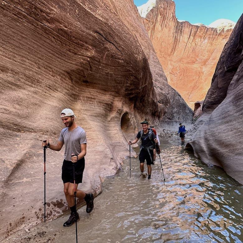 A group of hikers walk through a canyon filled with water