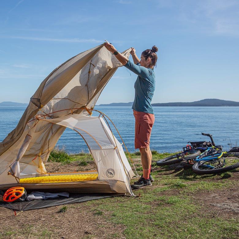 A woman puts the fly over the Tiger Wall tent next to the water with a bike behind her