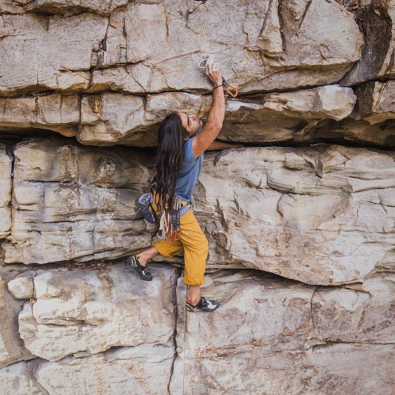 A man reaches up on a rock face to attach a quickdraw to a bolt