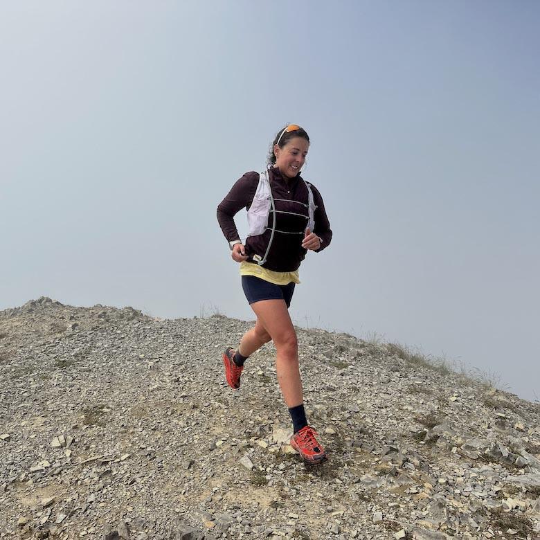A woman smiling and running down a rock face in the Hoka Speedgoat 2